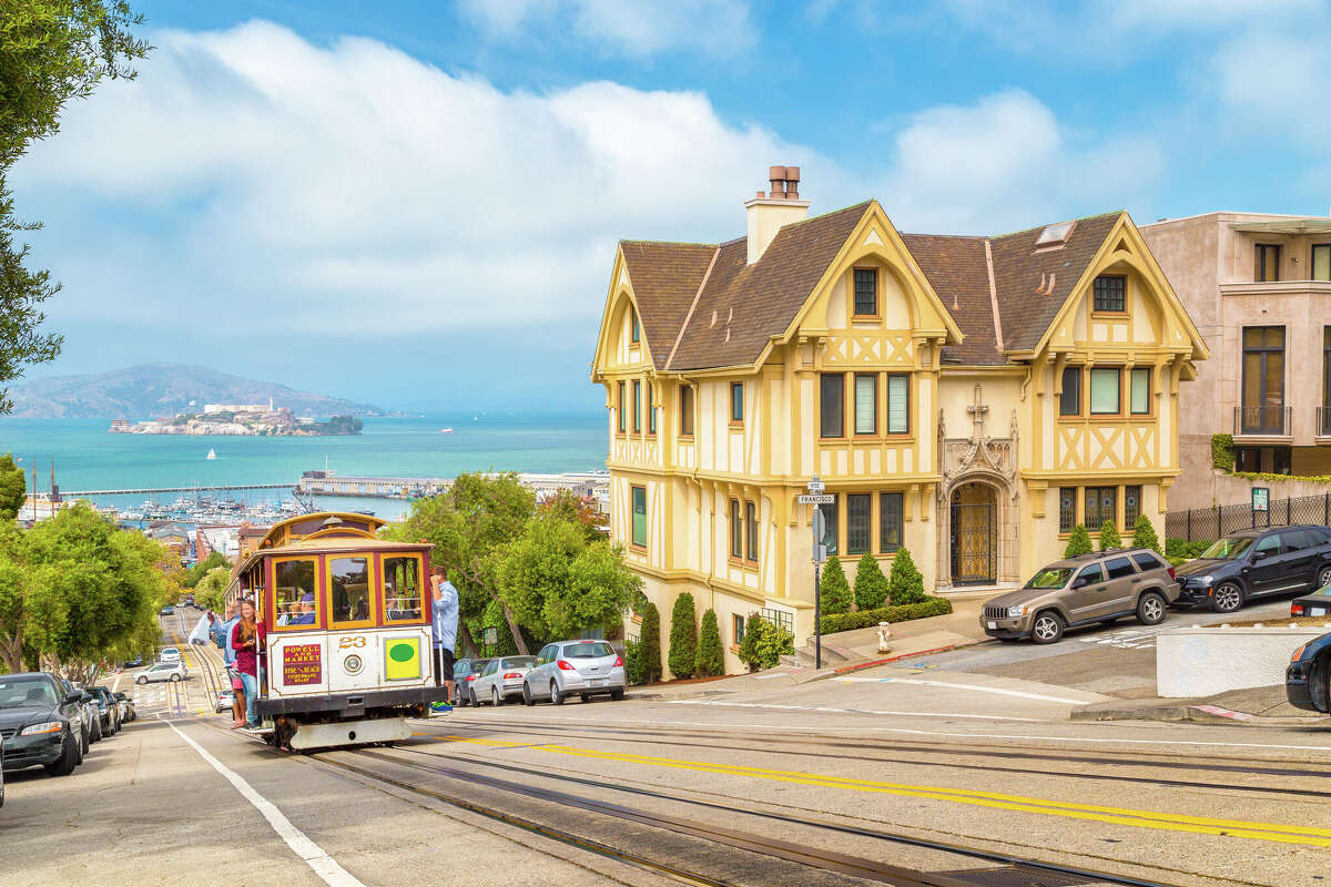 A Powell-Hyde cable car climbs a hill in San Francisco with Alcatraz Island in the background.
