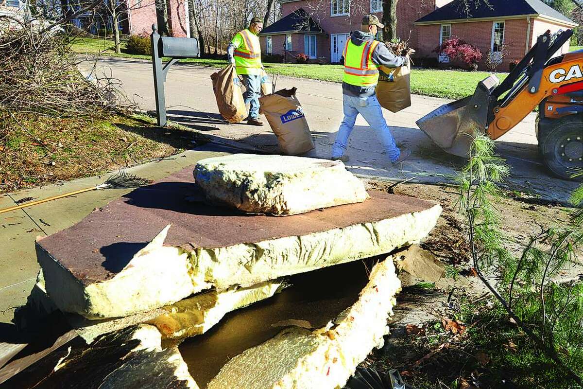Edwardsville public works employees clean up trees branches blown down in the County Club Estates neighborhood following an EF-3 tornado on Dec. 10. Stacks of insulation await removal in the neighborhood, foreground, from the Amazon warehouse to the west where six employees were killed. 