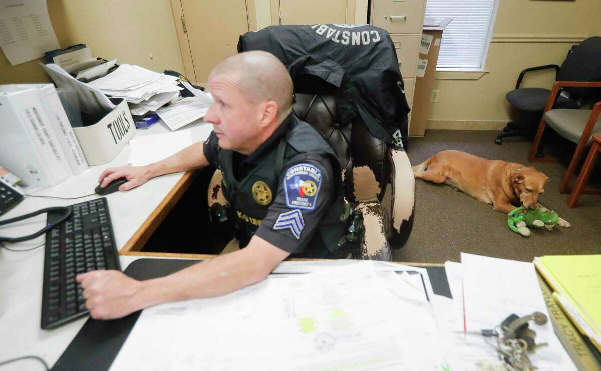 Sgt. Stephen Closson, with the Montgomery County Precinct 1 Constable’s office, works on his computer as his recently retired K9 partner, Barbie, plays with a toy, Tuesday, Feb. 1, 2022, in Willis.