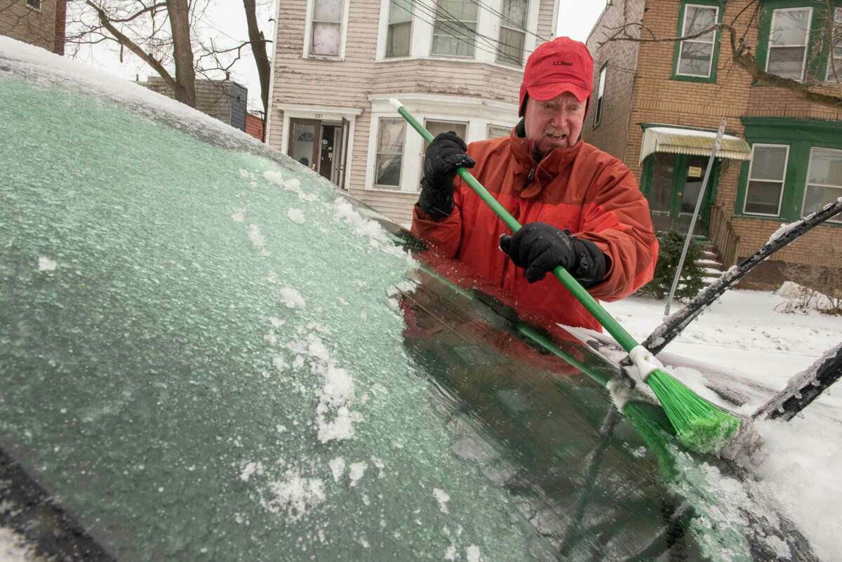Rick Garrison of Albany uses a broom to brush off the ice and snow he scrapped off his windshield during an icy snow storm on Friday, Feb. 4, 2022 in Albany, N.Y.