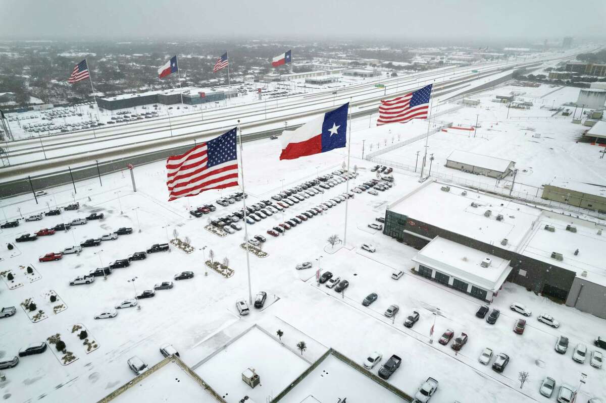 IRVING, TEXAS - FEBRUARY 03: In an aerial view, U.S. and Texas state flags fly over car dealerships as light traffic moves through snow and ice on U.S. Route 183 on February 03, 2022 in Irving, Texas. A winter storm blanketed much of Texas with snow, sleet and freezing rain, as it swept east, also affecting much of the midwest and eastern United States. (Photo by John Moore/Getty Images) *** BESTPIX ***