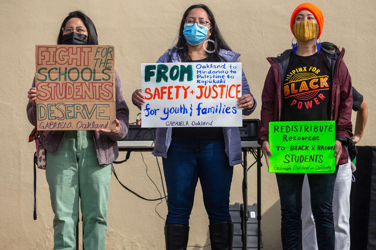 Left to right: Samantha Sipin, Claire Valderrama, and Jocelyn Deona, all of Gabriela Oakland hold signs calling for a stop to OUSD school closures at the start of the Oakland School Solidarity Rally and 4Peace Community Walk, on Saturday morning, Feb. 5, 2022.