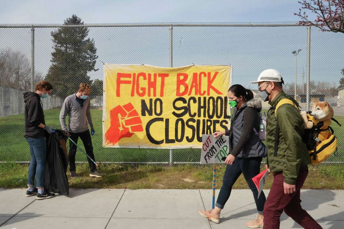Alicia Callejo-Black (left) and Devin Owen (second left) pick up litter near Prescott Elementary on Saturday, Feb. 5, 2022, in Oakland, Calif. Oakland school officials called a special meeting to discuss delaying the planned closure and consolidation of Oakland schools.