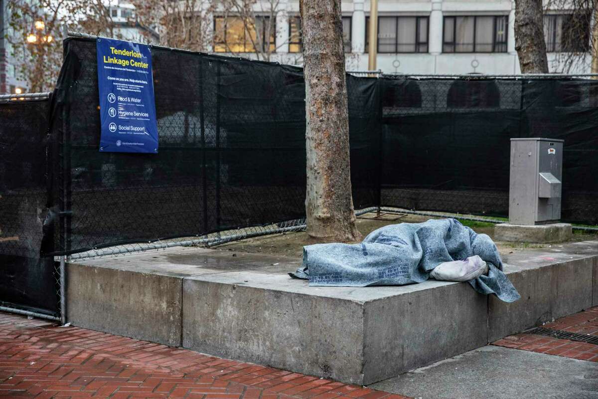 A person sleeps along a fence by the Tenderloin Linkage Center at United Nations Plaza in Janary. The center, part of the city’s Tenderloin emergency declaration, plans to provide people on the streets with treatment, housing and resources.