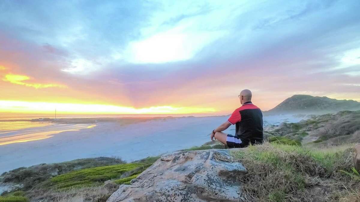 Rev. Immanuel Van Tonder meditates by the shore in South Africa. When he teaches his congregation meditation, he advises them to focus on calmness and don't worry about holding one image steadily in mind. He explains that a person can remain calm even while thoughts jump around like a monkey darting through tree branches.