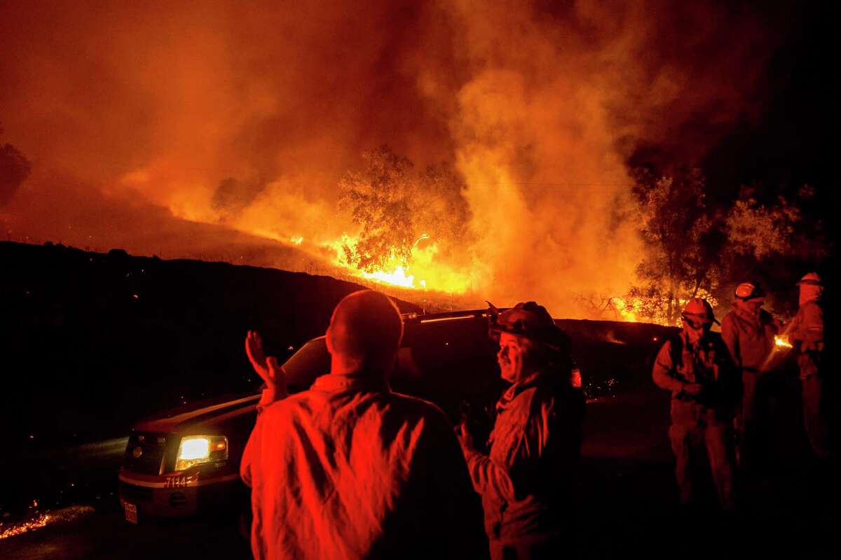 Firefighters confer while battling the Kincade Fire near Geyserville on Oct. 24, 2019. Portions of Northern California were dark that day after PG&E cut power to prevent more fires from sparking.