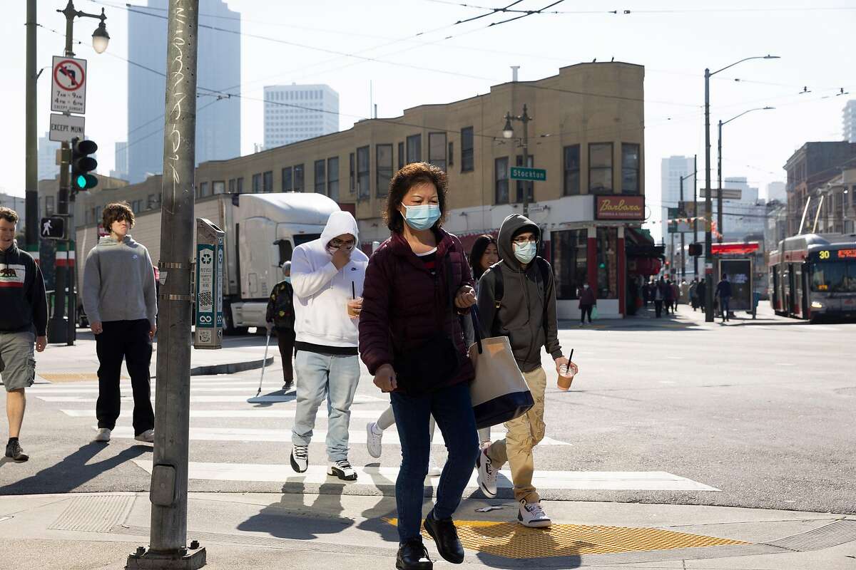 Pedestrians, some wearing masks, some not, walk along Columbus Avenue in the North Beach neighborhood in San Francisco, Calif., on Friday, February 4, 2022. As the Covid-19 virus becomes endemic, wearing masks may become a permanent cultural phenomenon long after mandates are lifted.