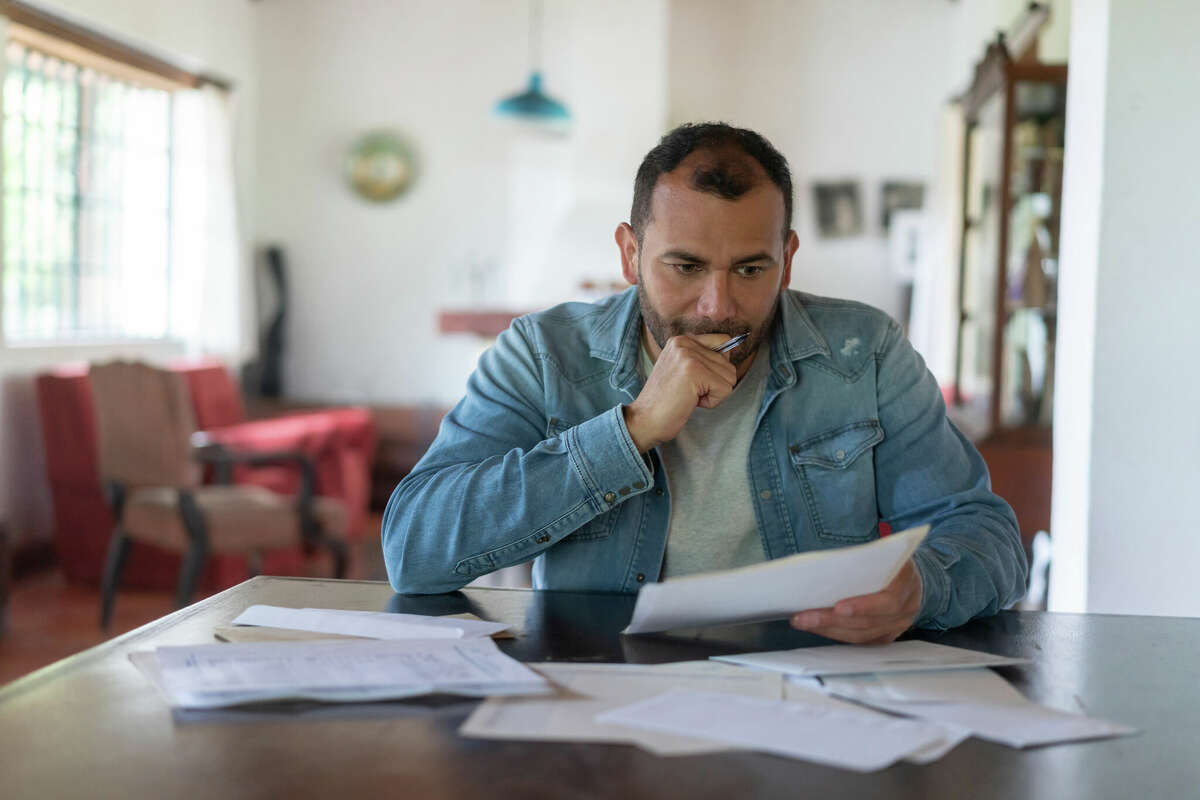 A man checks his home finances and looks worried while looking at utility bills. 