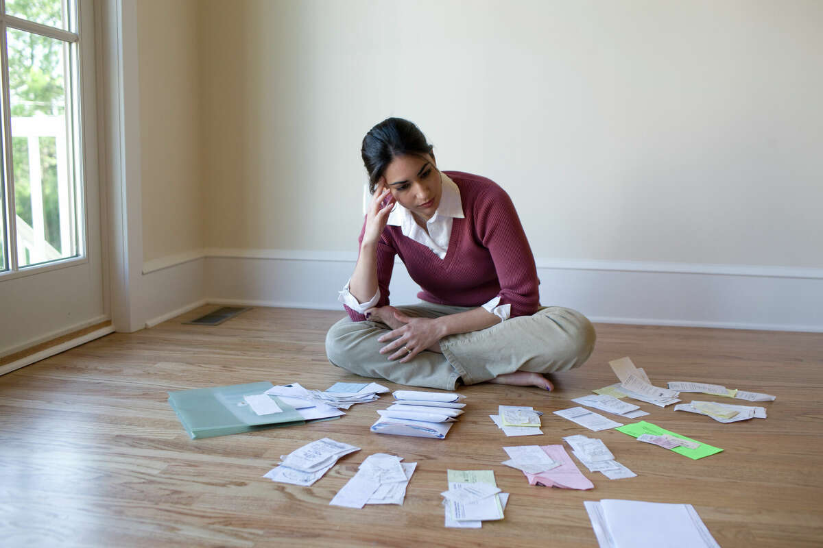 A woman sits on a floor looking at her bills. 