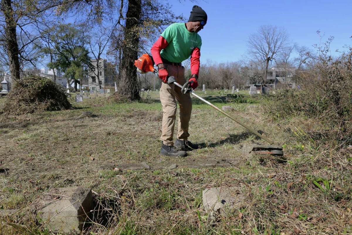 Charles Cook, VP of the Descendants of Olivewood Group, uses a weed whacker to clean up the overgrown area around grave plots at the historically black Olivewood cemetery Saturday, Feb. 5, 2022 in Houston, TX. Cook and some five other volunteers spent the morning weed whacking, raking leaves and doing general clean up across the cemetery.