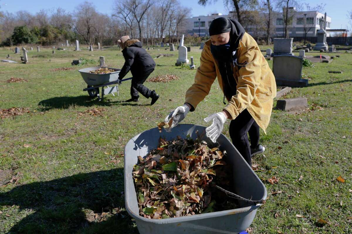 Volunteers Hailee Ammons, left, and Frances-Amanda Stallworth, right, rake and remove leaves as they and other volunteers clean up the area around grave plots at the historically black Olivewood cemetery Saturday, Feb. 5, 2022 in Houston, TX.