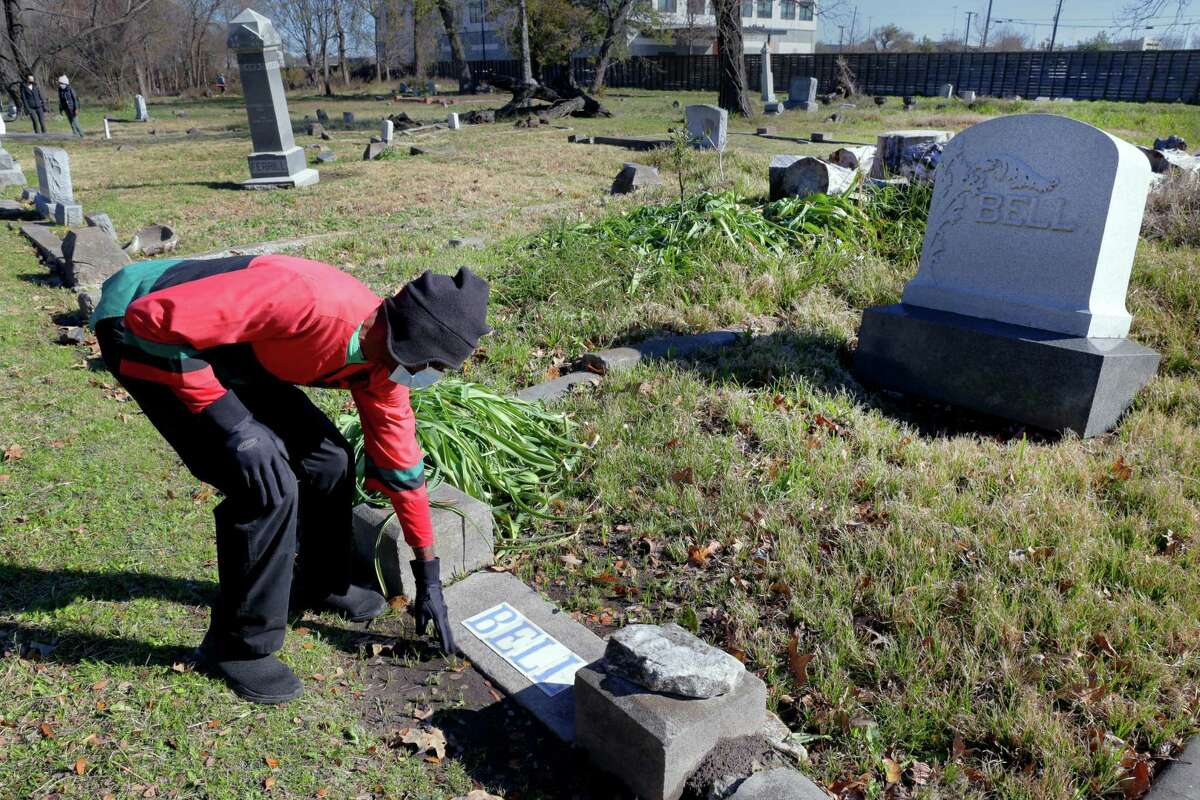 Charles Cook, VP of the Descendants of Olivewood Group, brushes away debris around the grave of John Brown Bell as he and other volunteers clean up the area around grave plots at the historically black Olivewood cemetery Saturday, Feb. 5, 2022 in Houston, TX. Bell, who was born in 1858 and came to Texas as a child with his enslaved mother, went on to accumulate a substantial fortune in Houston real estate.