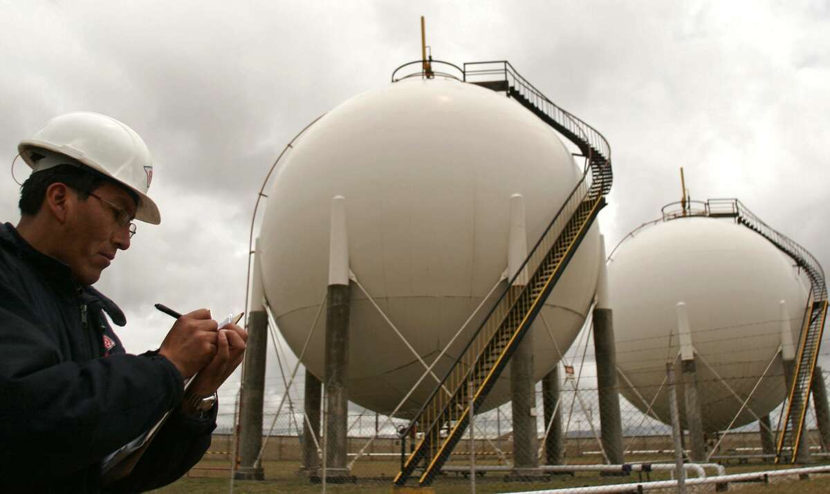 A worker takes notes next to natural gas storage tanks.