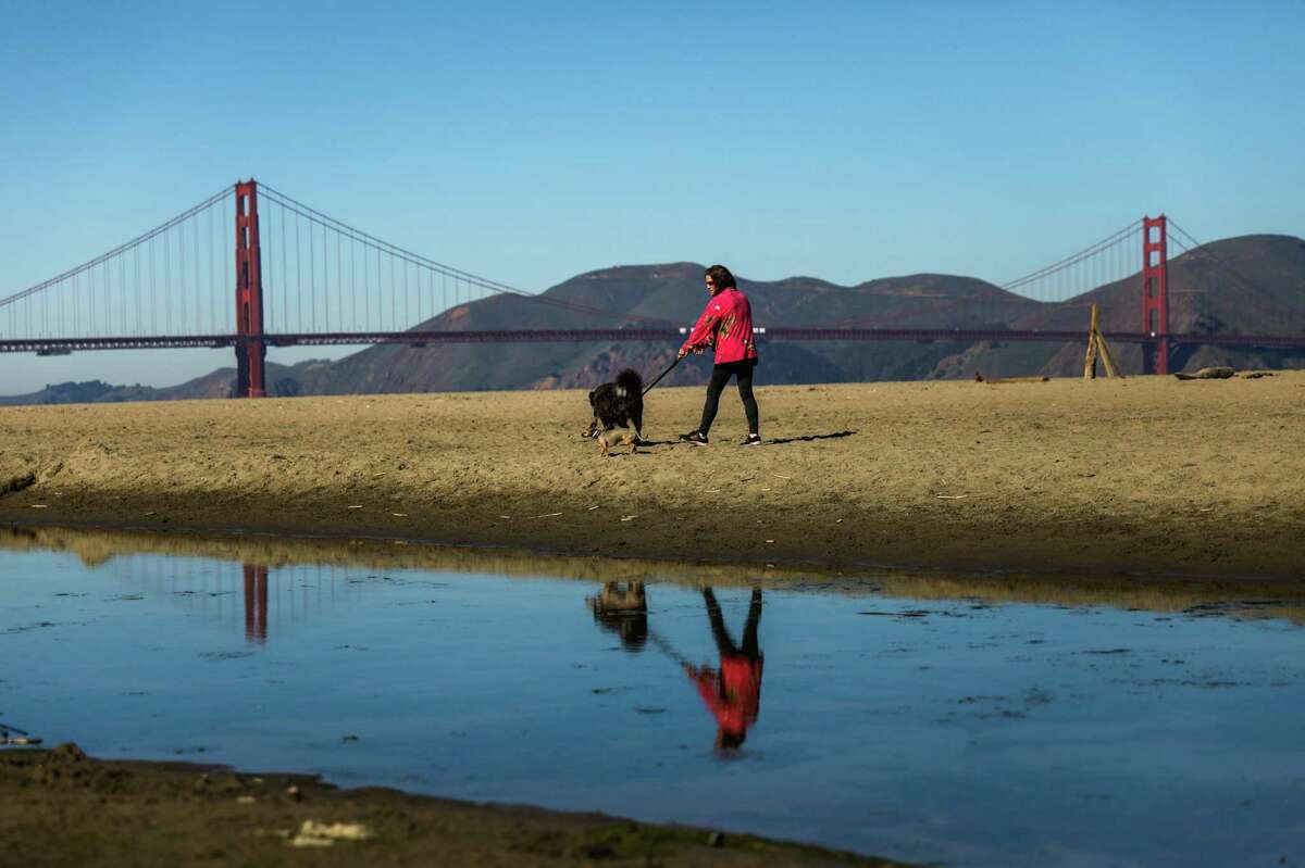 A woman walks a dog at Crissy Field on a warm day in San Francisco, Calif.
