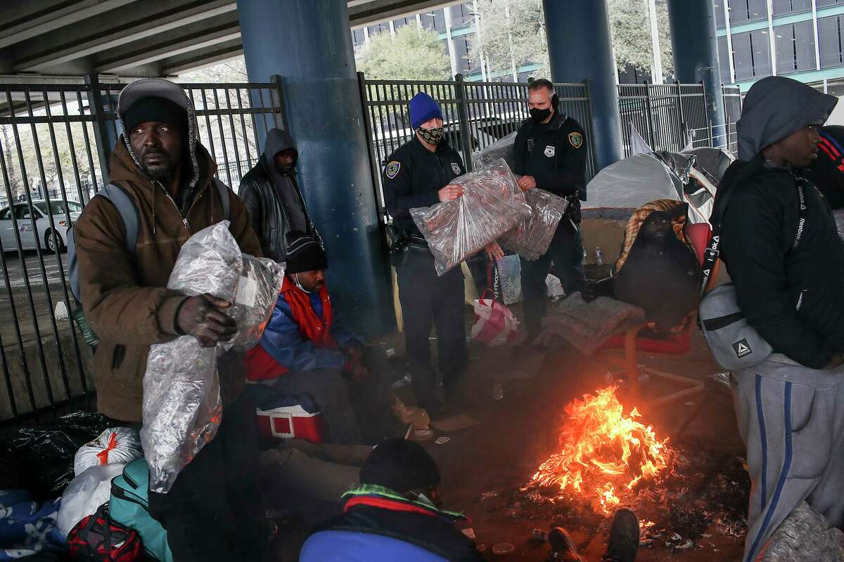 Houston Police officers Kenneth Bigger, center, and Aaron Day, center-right, hand out blankets to people as a winter storm continues to hit the area Tuesday, Feb. 16, 2021, under the elevated portion of I-45 in downtown Houston.