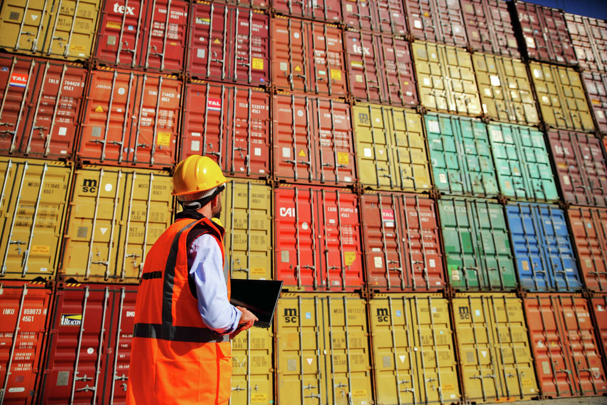 An engineer stands in front of a stack of cargo containers. 