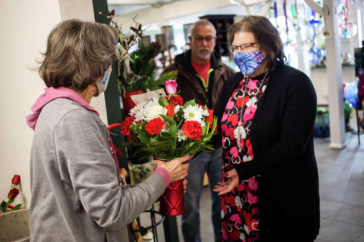 Carol Yeoman, left, hands a finished flower arrangement to her coworker, Lisa Theiss, right, before it is sold to Rodney Collins, center, on Valentine's Day, Monday, Feb. 14, 2022, at Village Green in Midland.
