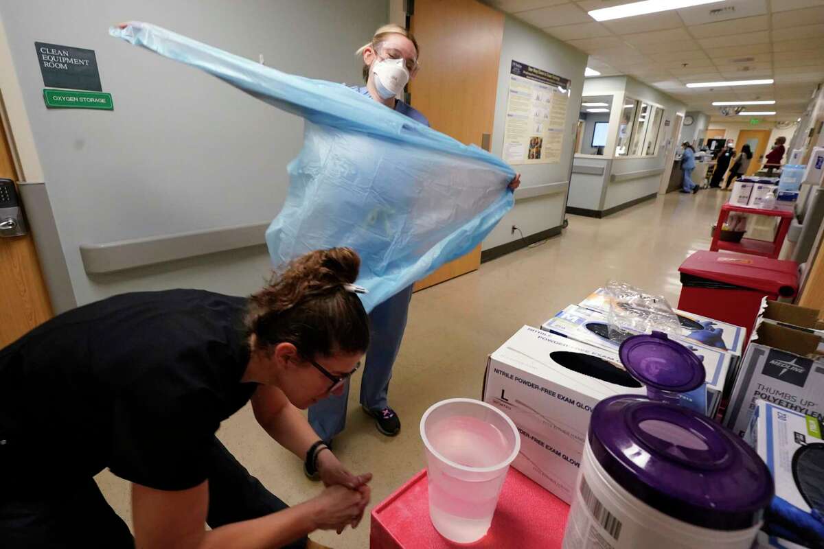 FILE - Registered nurse Jessalynn Dest, left, removes protective equipment and washes her hands after leaving a COVID-19 patient's room as speech therapist Sam Gibbs puts on safety clothing while preparing to see a patient in the acute care unit of Harborview Medical Center, Friday, Jan. 14, 2022, in Seattle. The coronavirus — the current variant or future ones that are sure to pop up — remains a dangerous germ. It is still infecting more than 130,000 Americans and killing more than 2,000 every day. Tens of millions of people remain vulnerable.