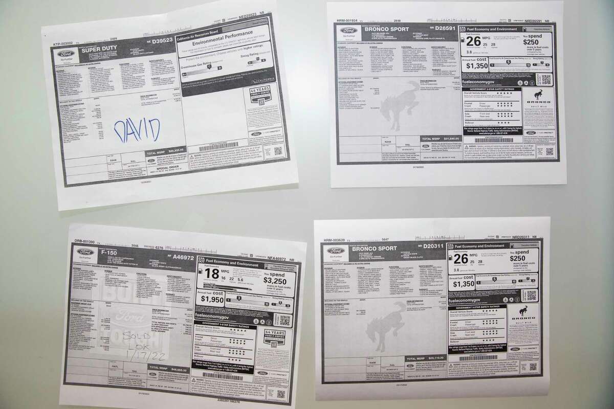 Window stickers for vehicles that will be delivered are hung on the glass wall at the dealership Thursday, Jan. 20, 2022, at Doggett Ford in Houston. Sales specialist David Claar said half of the vehicles on the glass door would be sold before they are delivered.