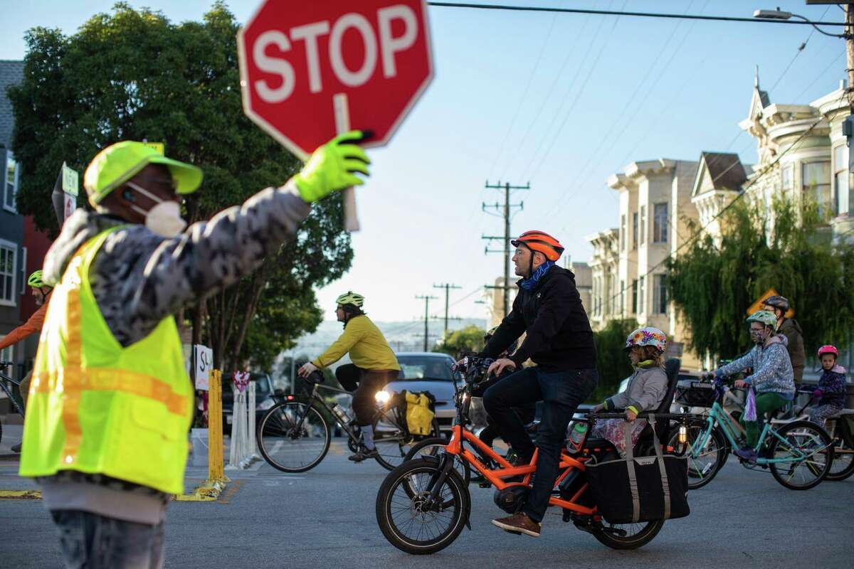 A crossing guard stops traffic as dozens of bicyclists commute together to school down Page Street in San Francisco.