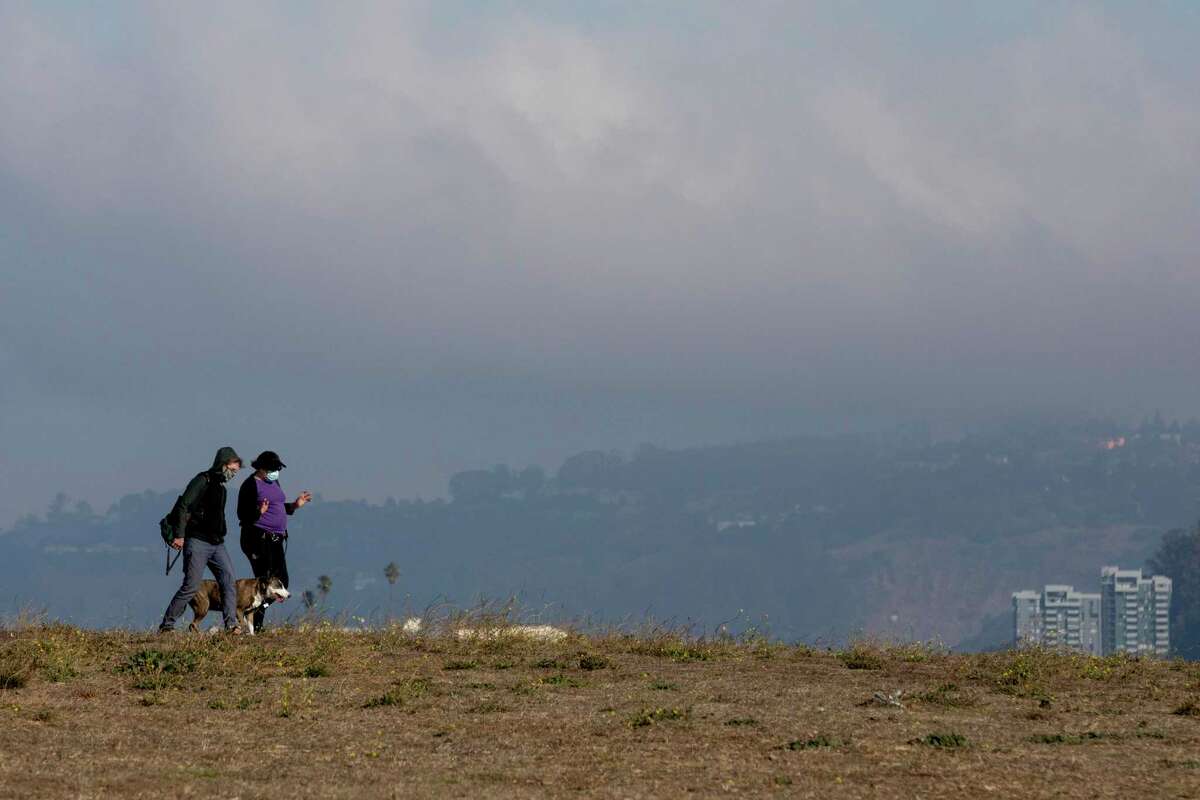 Two people bundle up while walking their dog under cloudy skies at the Berkeley Marina in Berkeley, Calif. Saturday, November 14, 2020. The monsoonal moisture flowing into Northern California from the coast of Mexico this week could bring a chance of wet and dry thunderstorms to the area starting Wednesday, meteorologists said.