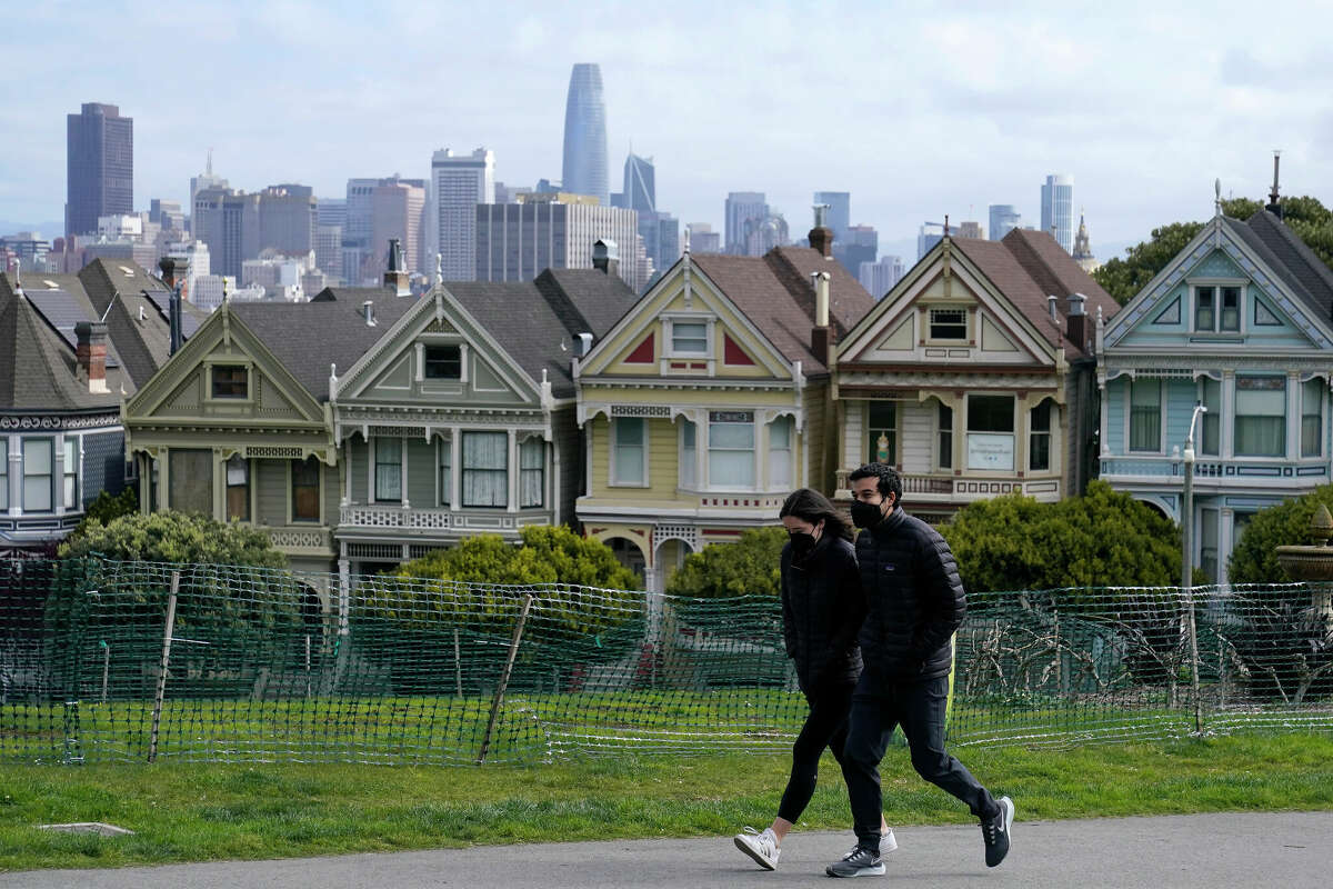 San Francisco has the highest COVID-19 case rate of any other county in California, but experts aren't concerned as cases and hospitalizations are still extremely low compared to what they were amid the winter surge. In this file photo, people wearing masks walk along at path in front of the "Painted Ladies," a row of historical Victorian homes, and the San Francisco skyline at Alamo Square Park during the coronavirus pandemic in San Francisco.