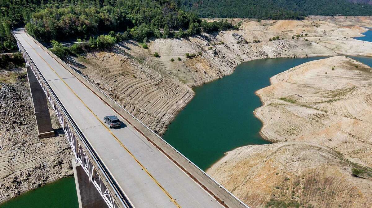 In this May 23, 2021, file photo, A vehicle crosses Enterprise Bridge over Lake Oroville’s dry banks last May, showing the low water level typical of many of California’s major reservoirs.