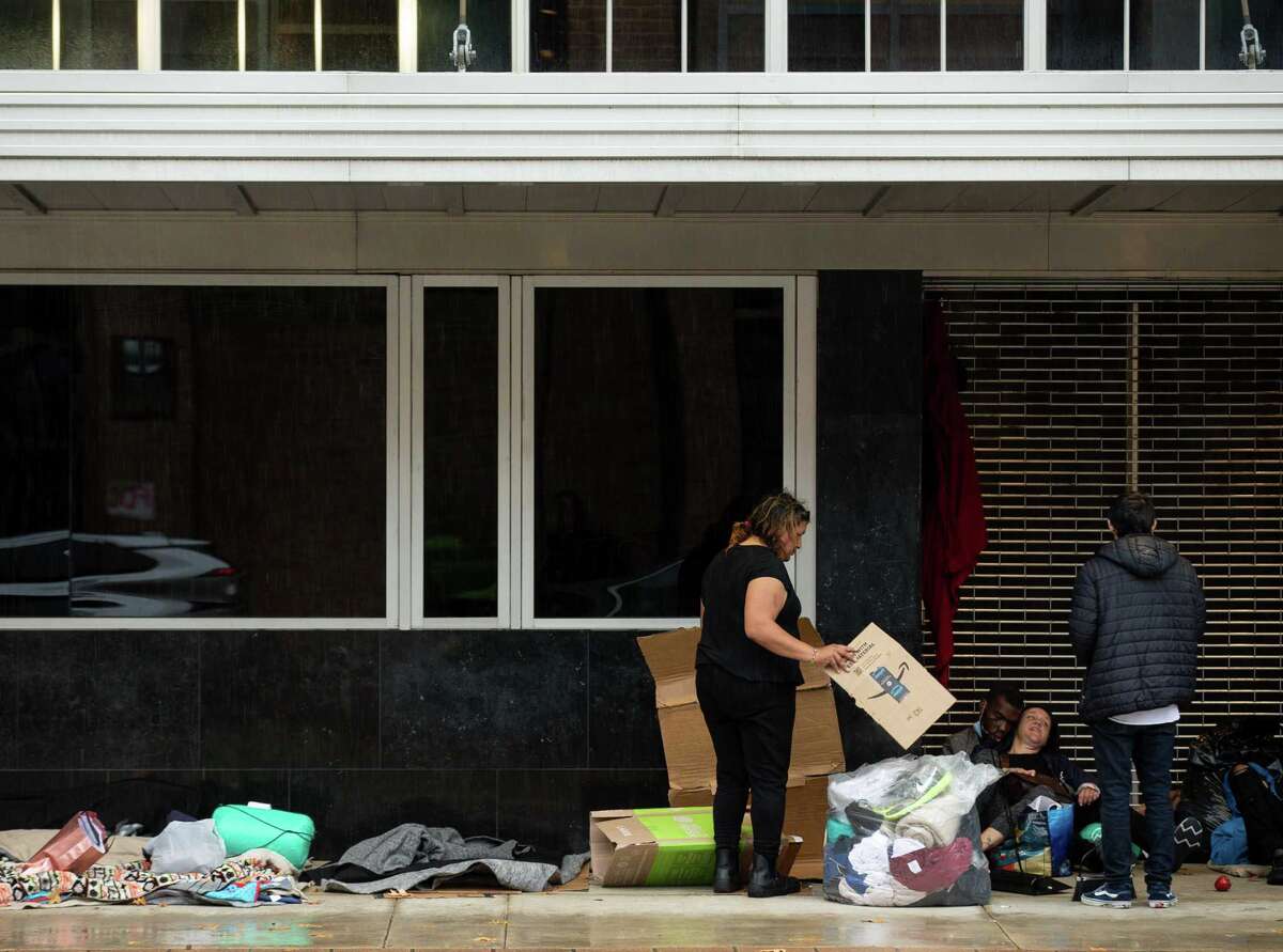 Kiki Aguero, center, and her friends settle in after moving to a sidewalk with a building overhang in order to shelter from the rain on Jan. 31, 2022.
