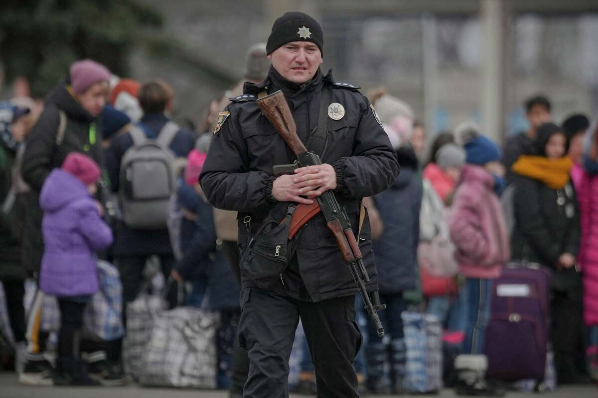 A Ukrainian police officer carrying an assault rifle walks on a platform backdropped by people waiting for a Kiev bound train in Kostiantynivka, the Donetsk region, eastern Ukraine, Thursday, Feb. 24, 2022. Russia launched a wide-ranging attack on Ukraine on Thursday, hitting cities and bases with airstrikes or shelling, as civilians piled into trains and cars to flee. (AP Photo/Vadim Ghirda)
