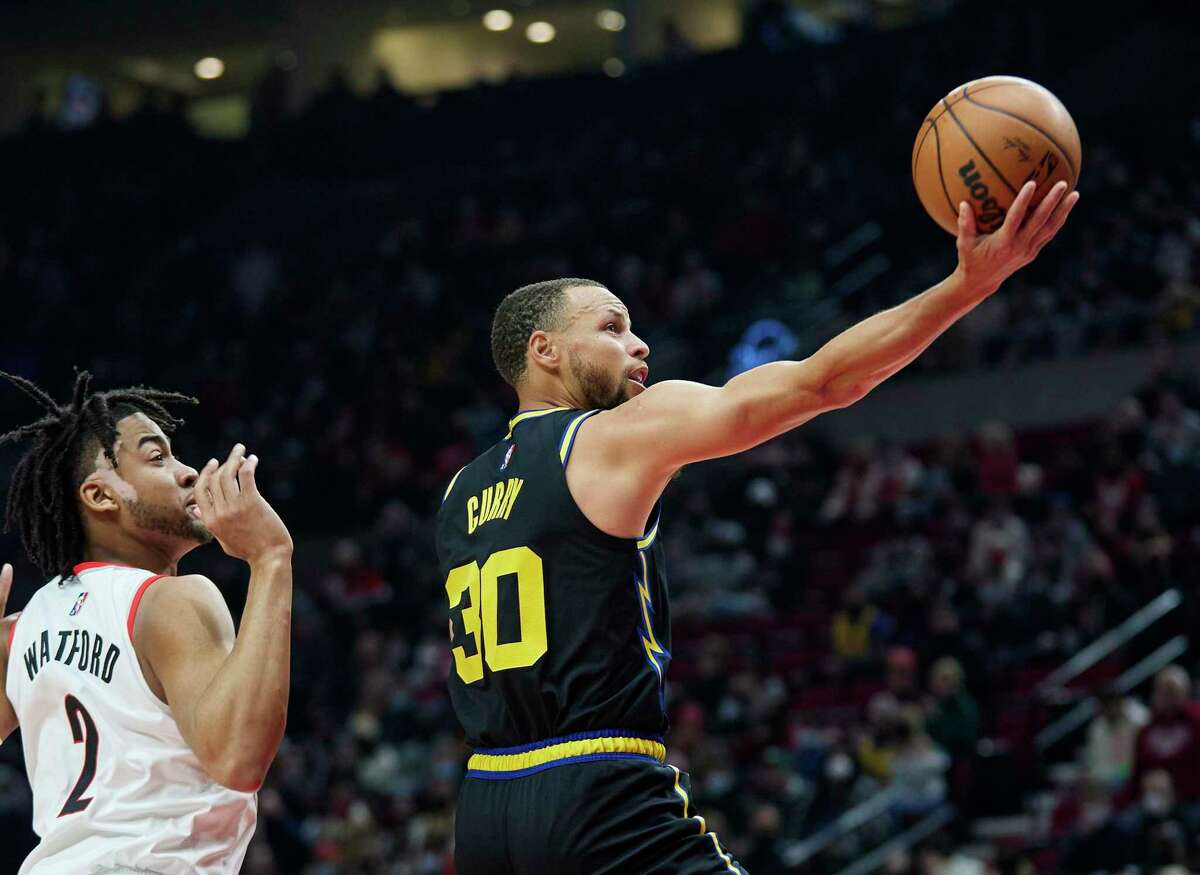 Golden State Warriors guard Stephen Curry, right, shoots in front of Portland Trail Blazers forward Trendon Watford during the first half of an NBA basketball game in Portland, Ore., Thursday, Feb. 24, 2022. (AP Photo/Craig Mitchelldyer)