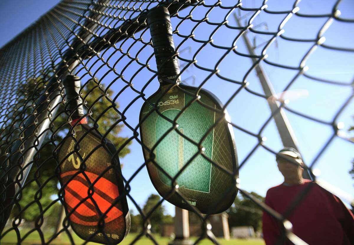 Pickleball rackets hang on the fencing as players wait to play at Unity Park in Trumbull, Conn. on Tuesday, September 29, 2021.