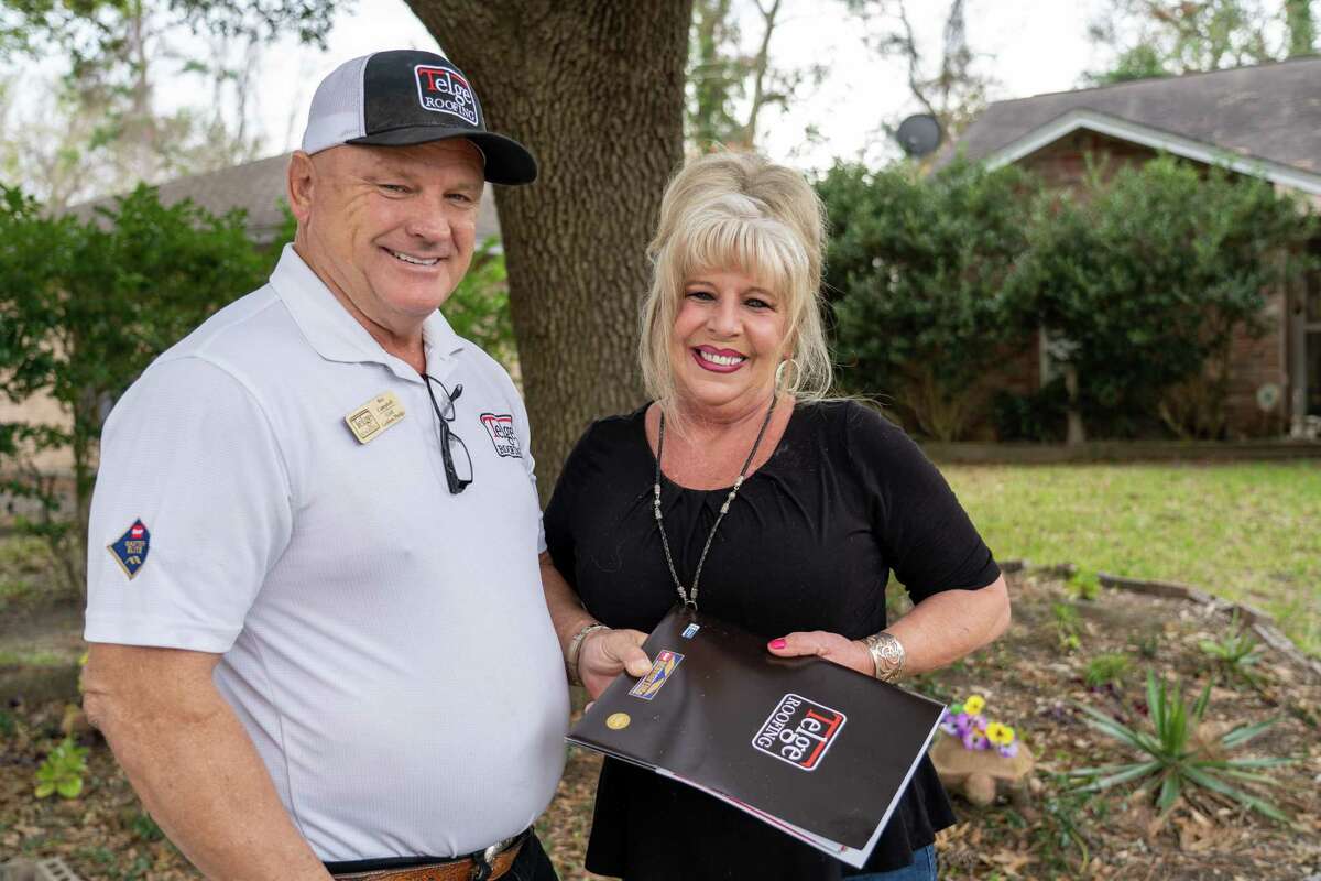 Roy Campbell hands Donna Hughes the paperwork for her new roof. The warranty for the Timberline roof is 50 years.