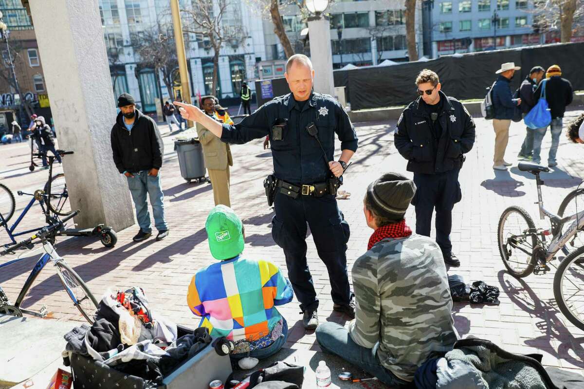 Police officers Mitchinson (left) and Ryan Doherty talk to people in a spot frequented by drug users outside the linkage center at Civic Center Plaza.