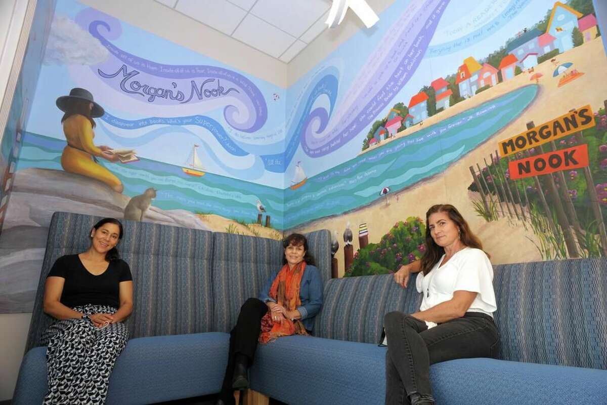From left, artists Melissa Imossi, Linda Marino and Hilary Griffin sit under the mural they painted in Morgan’s Nook of the Scranton Library, in Madison, Conn., Oct. 23, 2020.