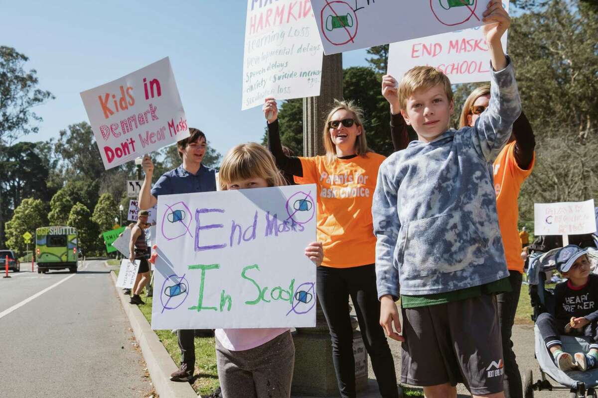 Ellie Quigley (left) and her brother Dominic hold signs in front of their mom Corinne Quigley at the Parents for Mask Choice rally in San Francisco’s Golden Gate Park.