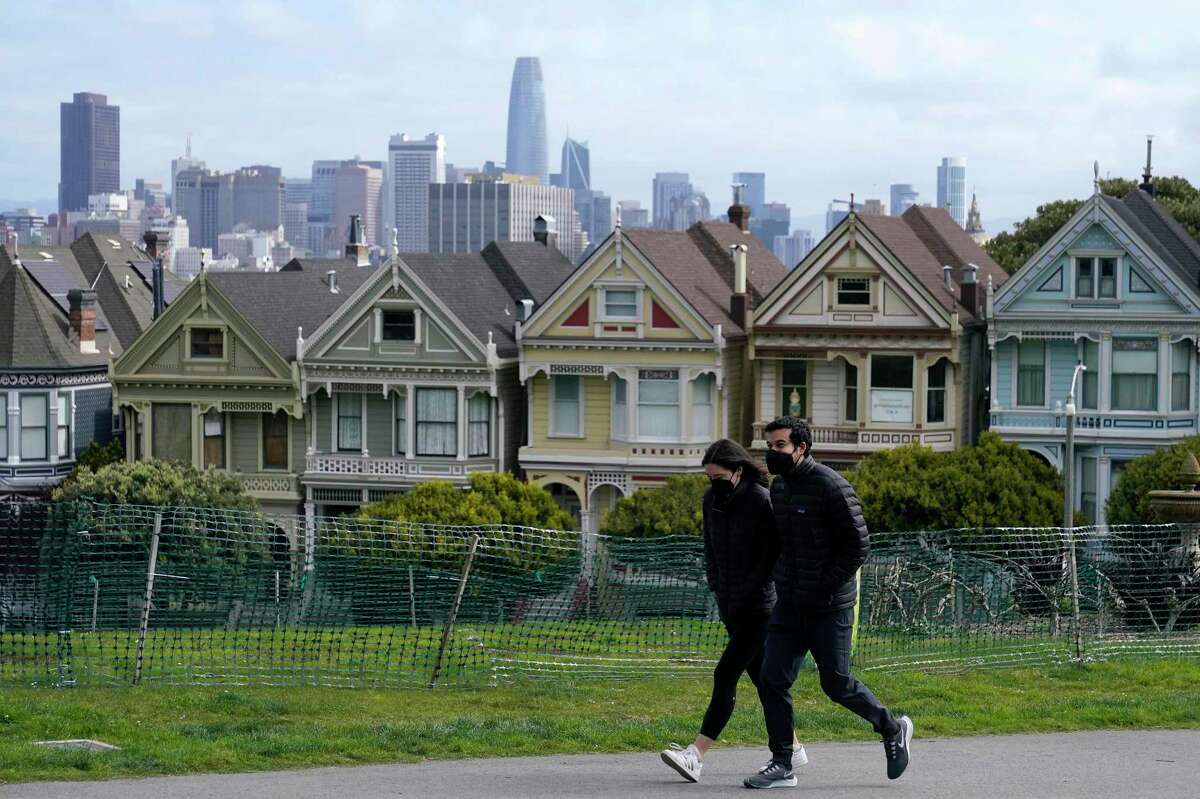 Pedestrians wear masks walking by San Francisco’s historic “Painted Ladies” historical homes. California’s latest switch says that even unvaccinated people no longer must wear masks in most indoor public settings.