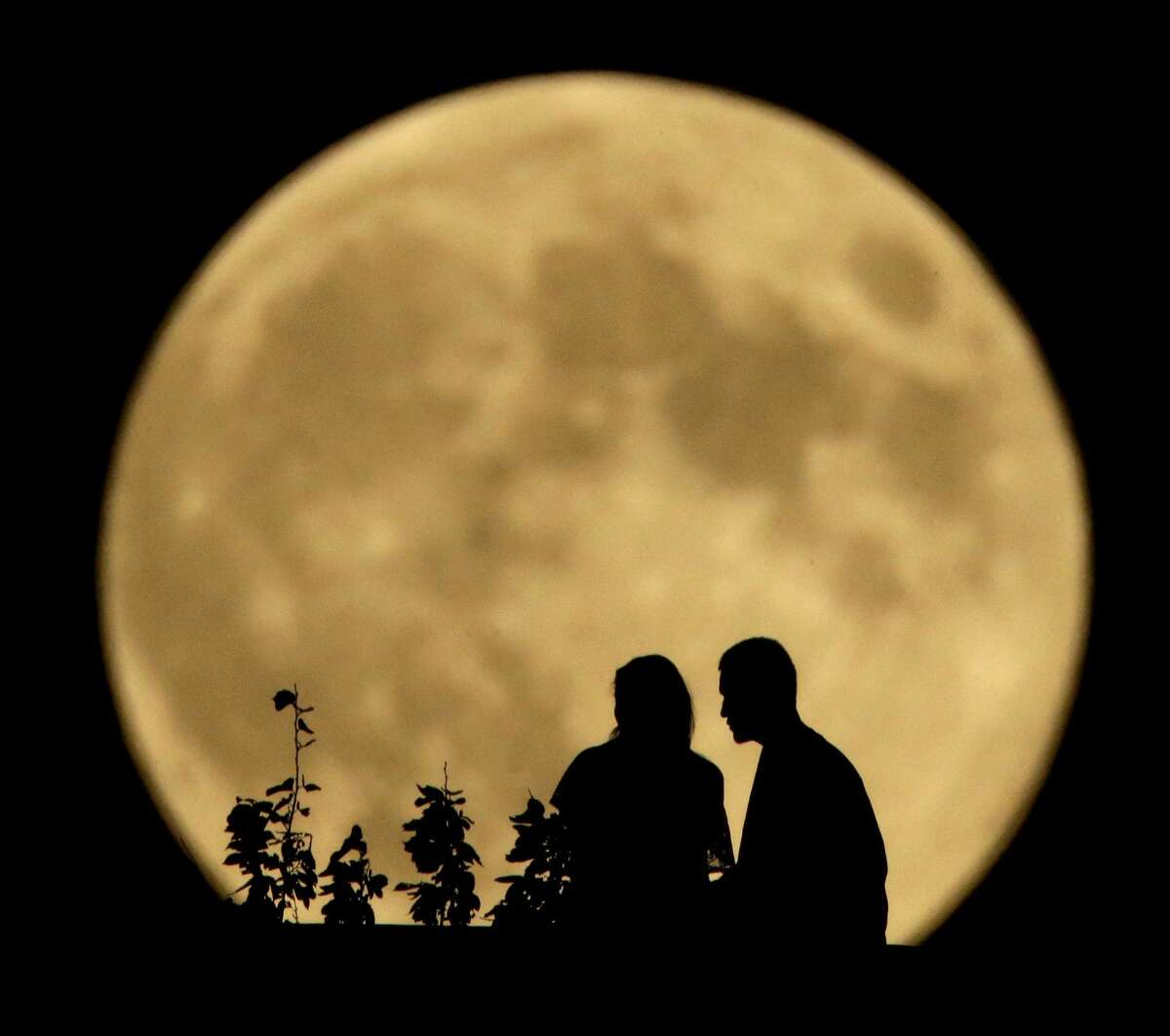 A couple sits on a bluff overlooking the Missouri River as the full moon rises in the distance Monday, Sept. 8, 2014, in Kansas City, Mo. Monday night's full moon, also known as a Harvest Moon, will be the third and final "supermoon" of 2014. The phenomenon, which scientists call a "perigee moon," occurs when the moon is near the horizon and appears larger and brighter than other full moons. (AP Photo/Charlie Riedel)