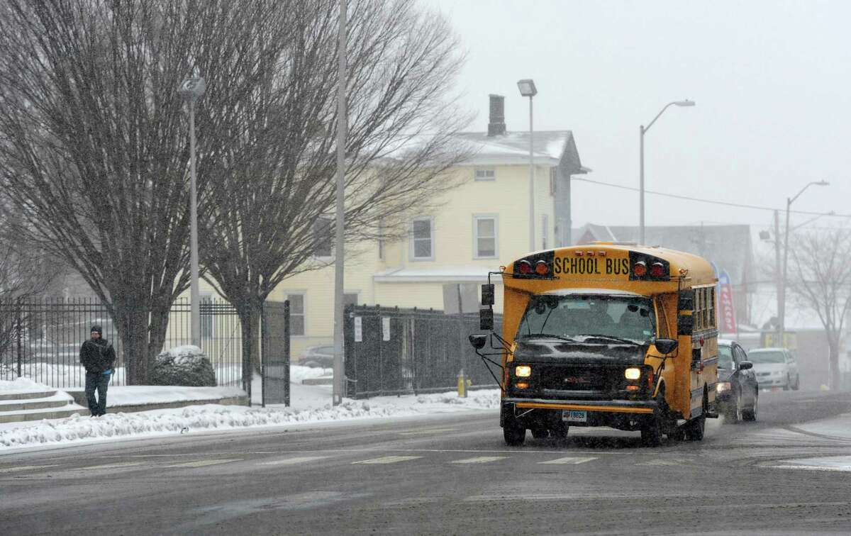 A school bus makes its way down State Street as pedestrians brave the wind and snow in Bridgeport, Conn. on Monday, Feb. 8, 2016.