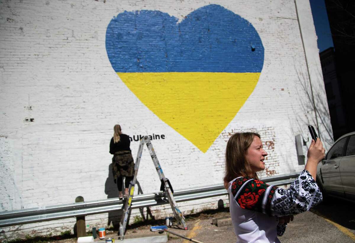 Iryna Petrovska Marchiano, president for Ukrainian American Cultural Club of Houston records herself presenting the Ukrainian community with a mural with the Ukrainian flag, Monday, Feb. 28, 2022, in Houston. The artist working on the mural is Shelbi Nicole.
