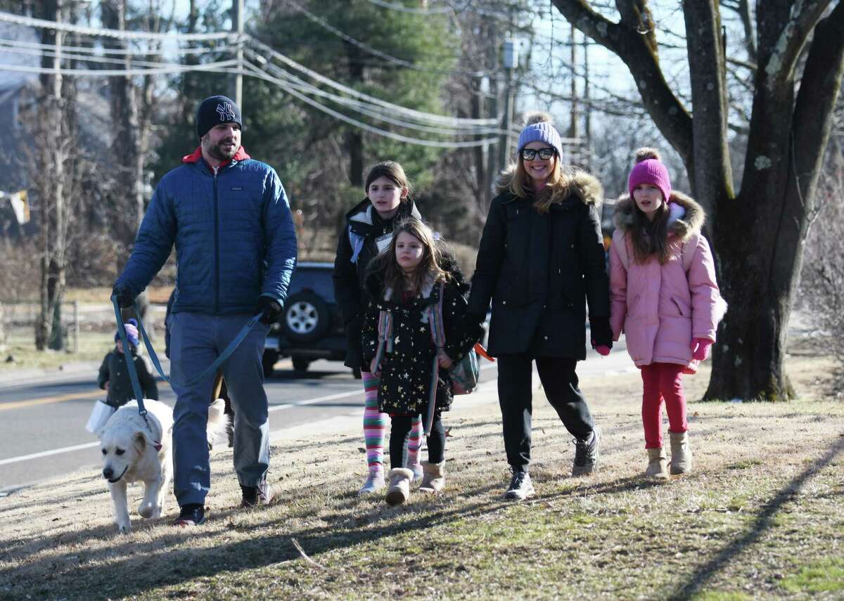 Darien parents Matt and Catherine Palazola pick up their children, fourth-grader Emma, kindergartener Lila, and second-grader Sadie, from Holmes Elementary School in Darien, Conn. Monday, Feb. 28, 2022. The state’s broad school-based mask mandate was lifted Monday, giving students and their parents the option of whether to wear masks in school.