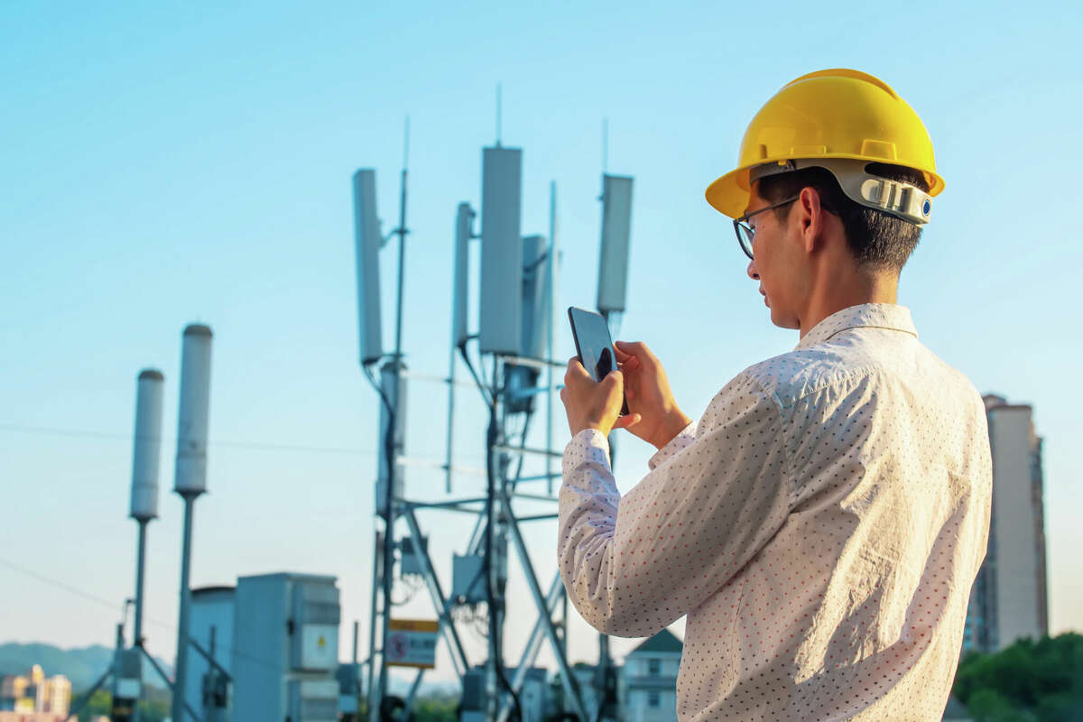 Engineer holding mobile phone testing the communications tower