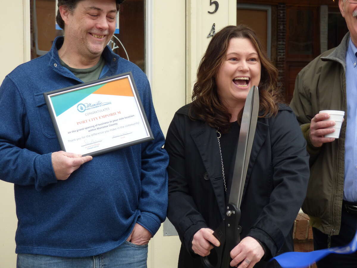 Anita Shaffer cuts the ribbon at the recently reopened store she co-owns with Patrick Shaffer pictured holding a certificate from the Manistee Area Chamber of Commerce on Wednesday morning.