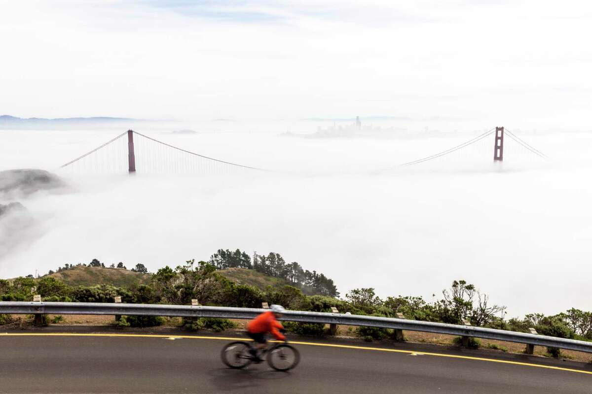 A cyclist descends Conzelman Road in the Marin Headlands as the Golden Gate Bridge is seen surrounded by a layer of fog in Sausalito, California Wednesday, March 2, 2022.