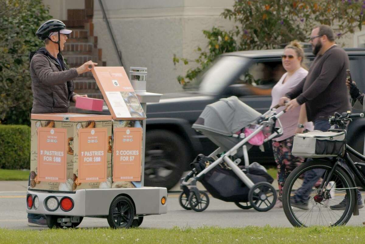 A customer retrieves a box of Bake Sum pastries from a Tortoise robot.