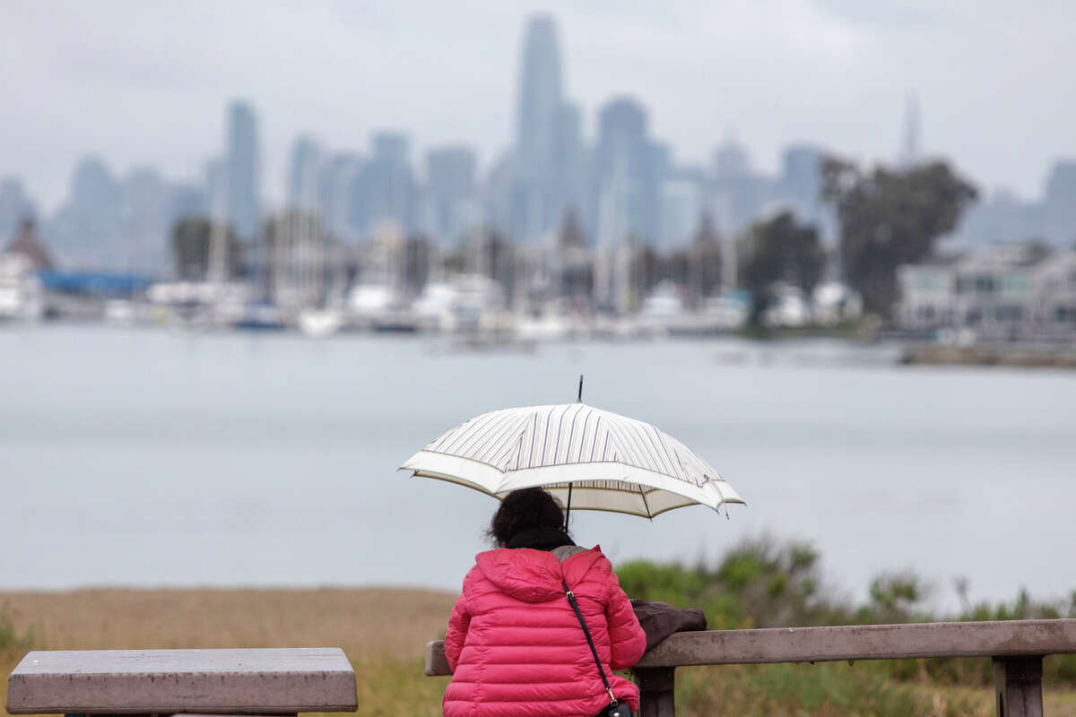 A woman sits under an umbrella during a light rainfall in Alameda, Calif. on Mar. 3, 2022.