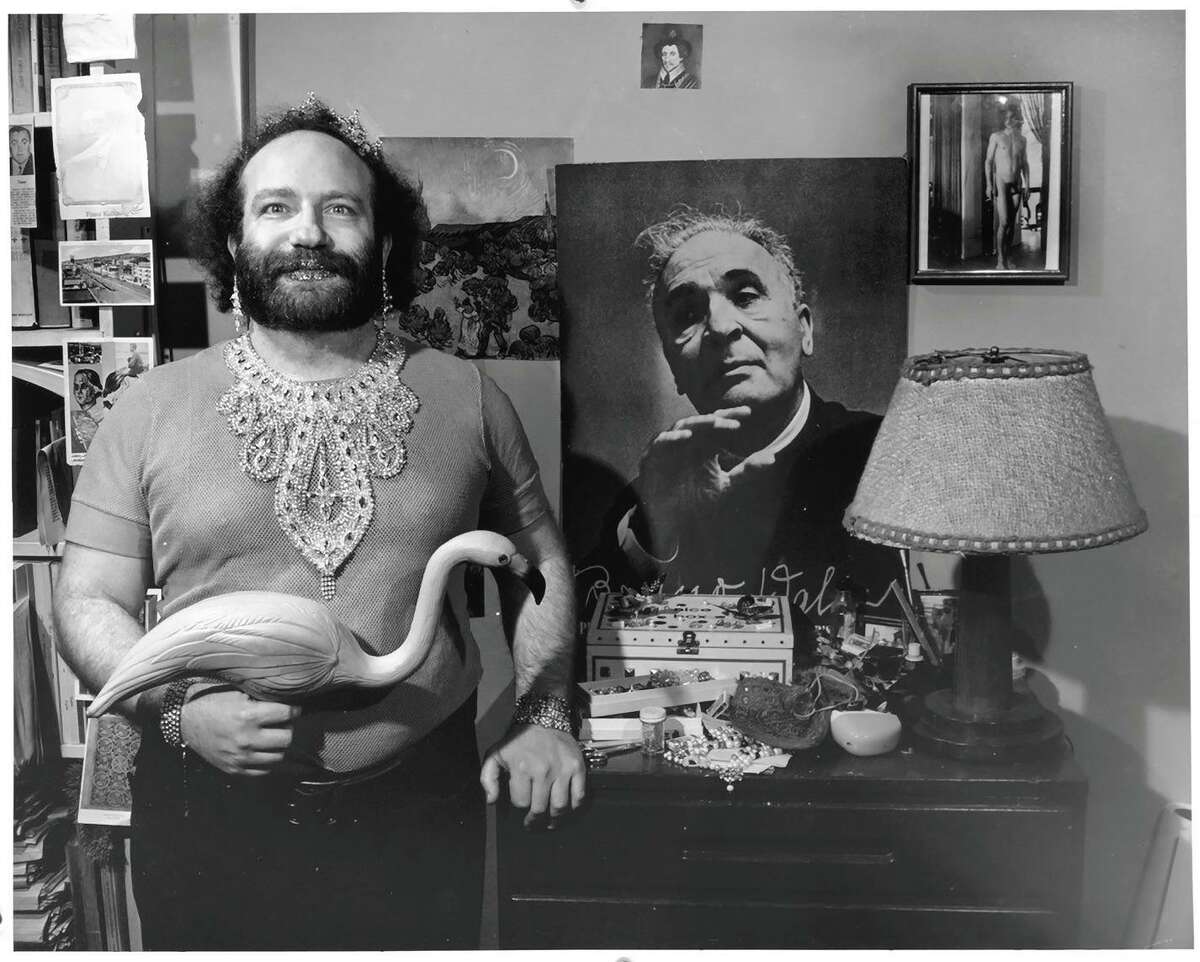 David Melnick in a 1974 art gallery image titled “Nice, with glitter lips, rhinestone necklace, pink flamingo, and Bruno Walter” in Berkeley. “Nice” was a nickname Melnick adopted.