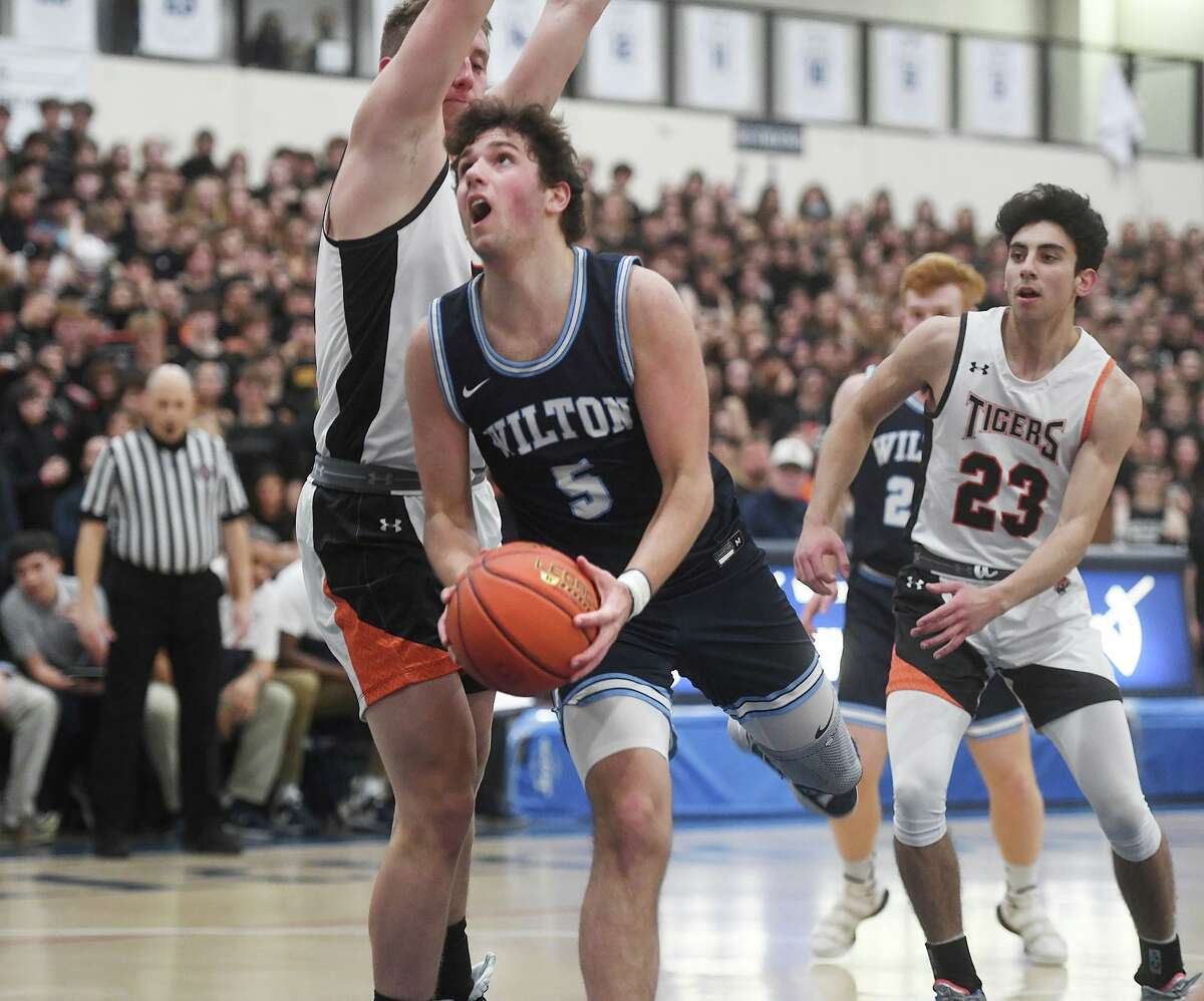 Wilton’s Kevin Hyzy drives to the basket around Ridgefield defender Dylan Veillette during the FCIAC championship on March 3.