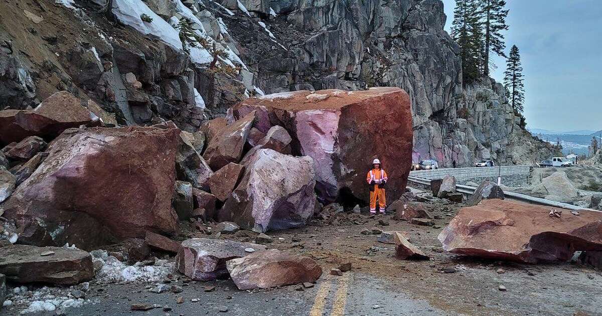 A man stands in front of a massive boulder blocking Highway 50 at Echo Summit.
