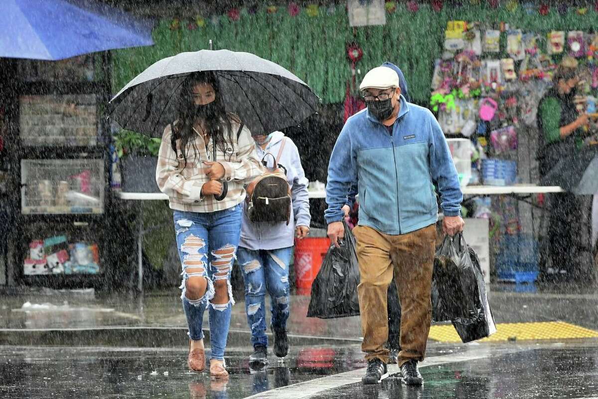 People cross a street under heavy rain in Los Angeles, Calif. on Oct. 25, 2021. (Photo by Frederic J. Brown/AFP via Getty Images)