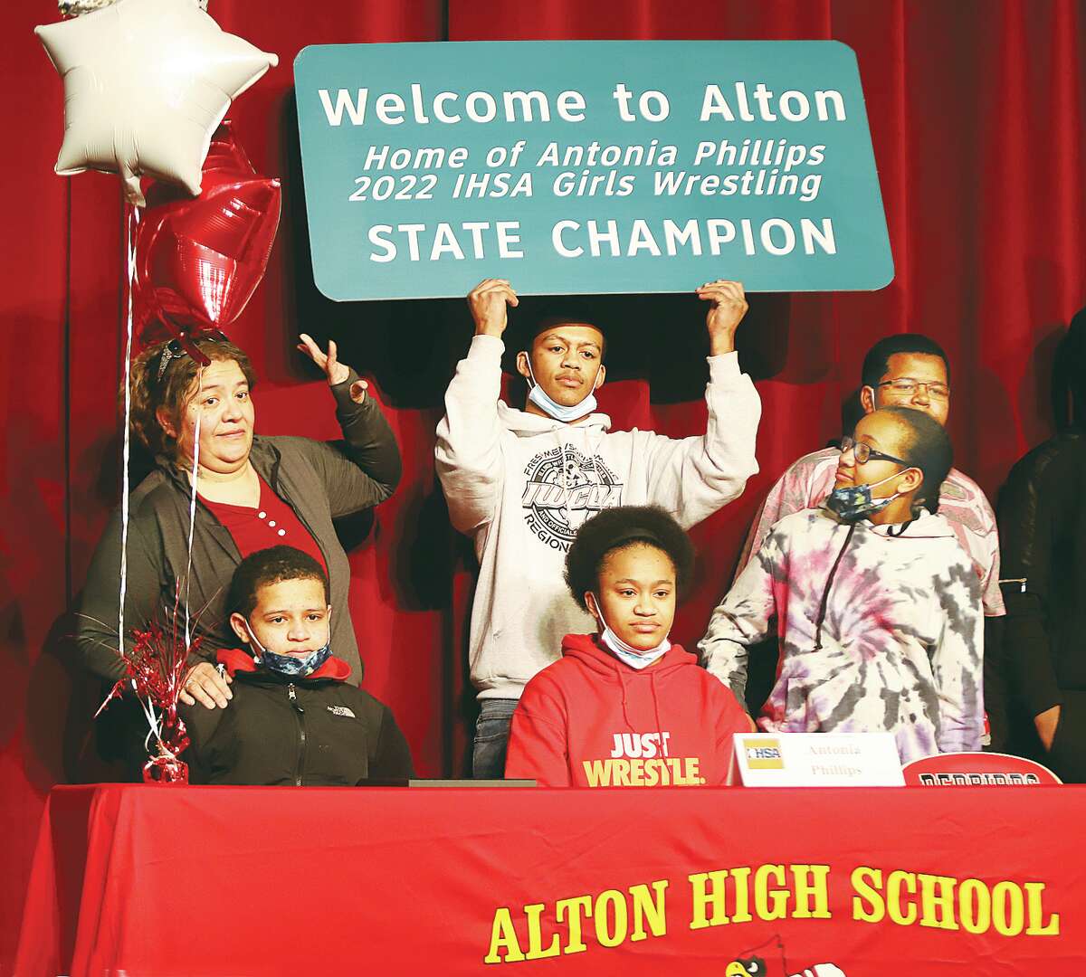 John Badman|The Telegraph IHSA state champion wrestler Antonia Phillips, center, poses for a picture with her family, including her mother, Lupe Phillips, left, as they hold a sign celebrating her accomplishment. Alton Mayor David Goins wants to put similar signs up on each highway entry point into the city.